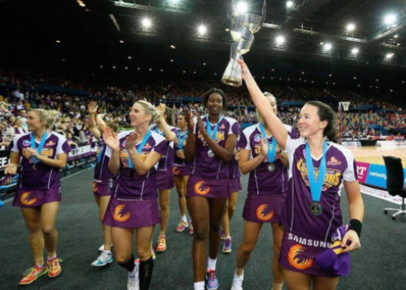 Caitlyn Strachan lifting the championship trophy on the Firebirds premiership lap of honour, wearing a Champions tee.