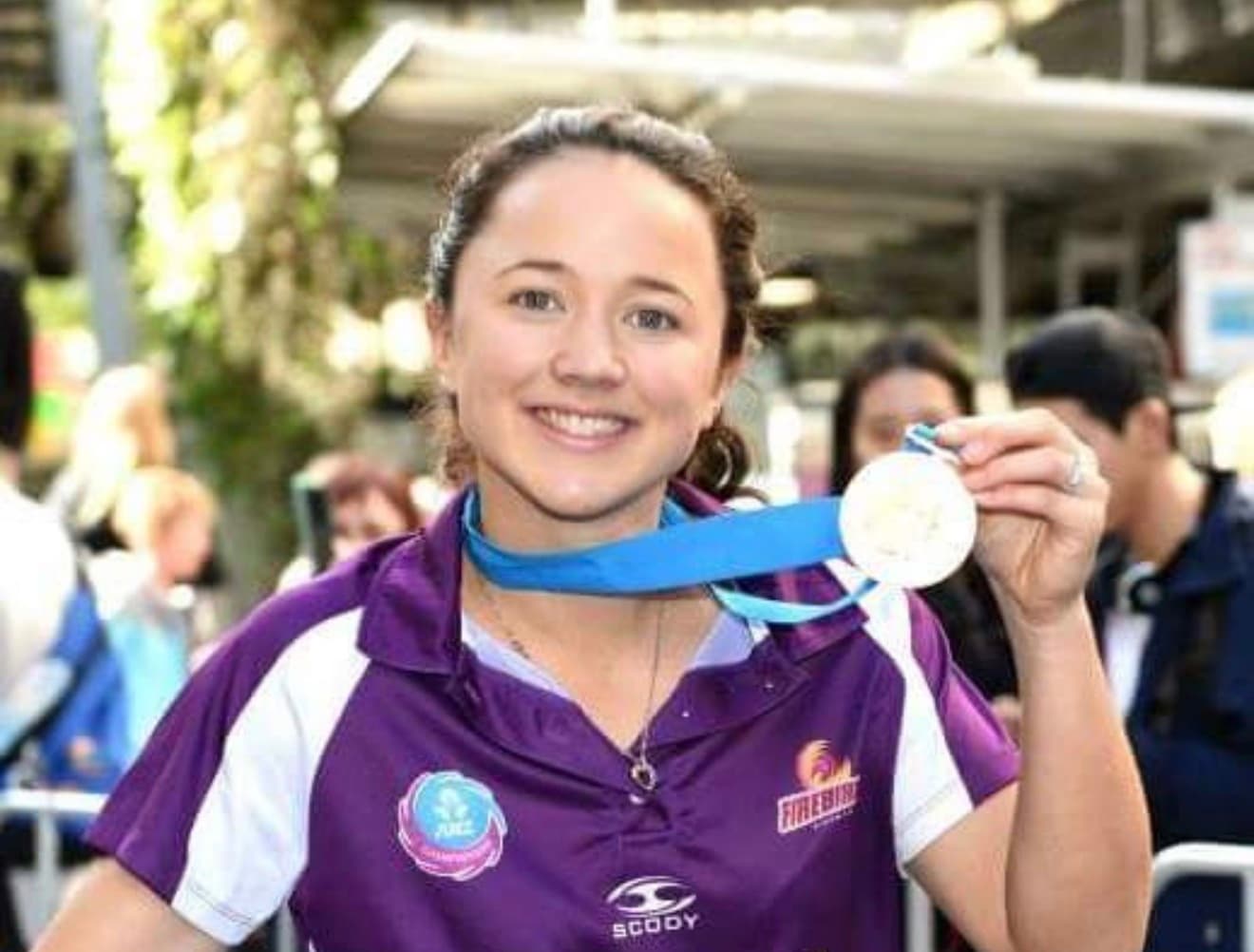 Close-up portrait of Caitlyn Strachan smiling and holding up her ANZ Champions medal in a Firebirds polo