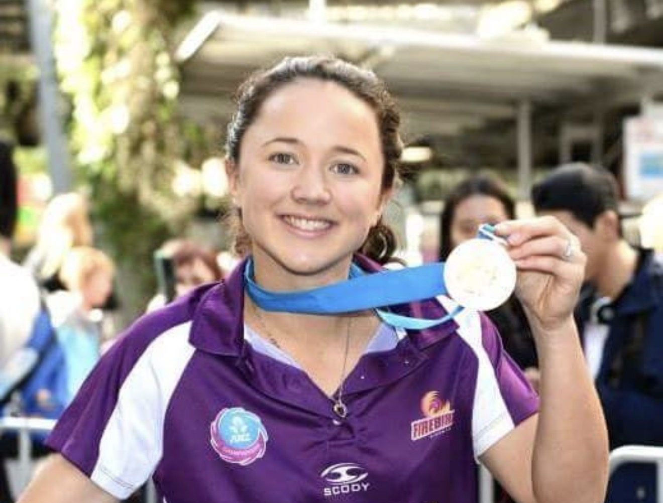 Close-up portrait of Caitlyn Strachan smiling and holding up her ANZ Champions medal in a Firebirds polo